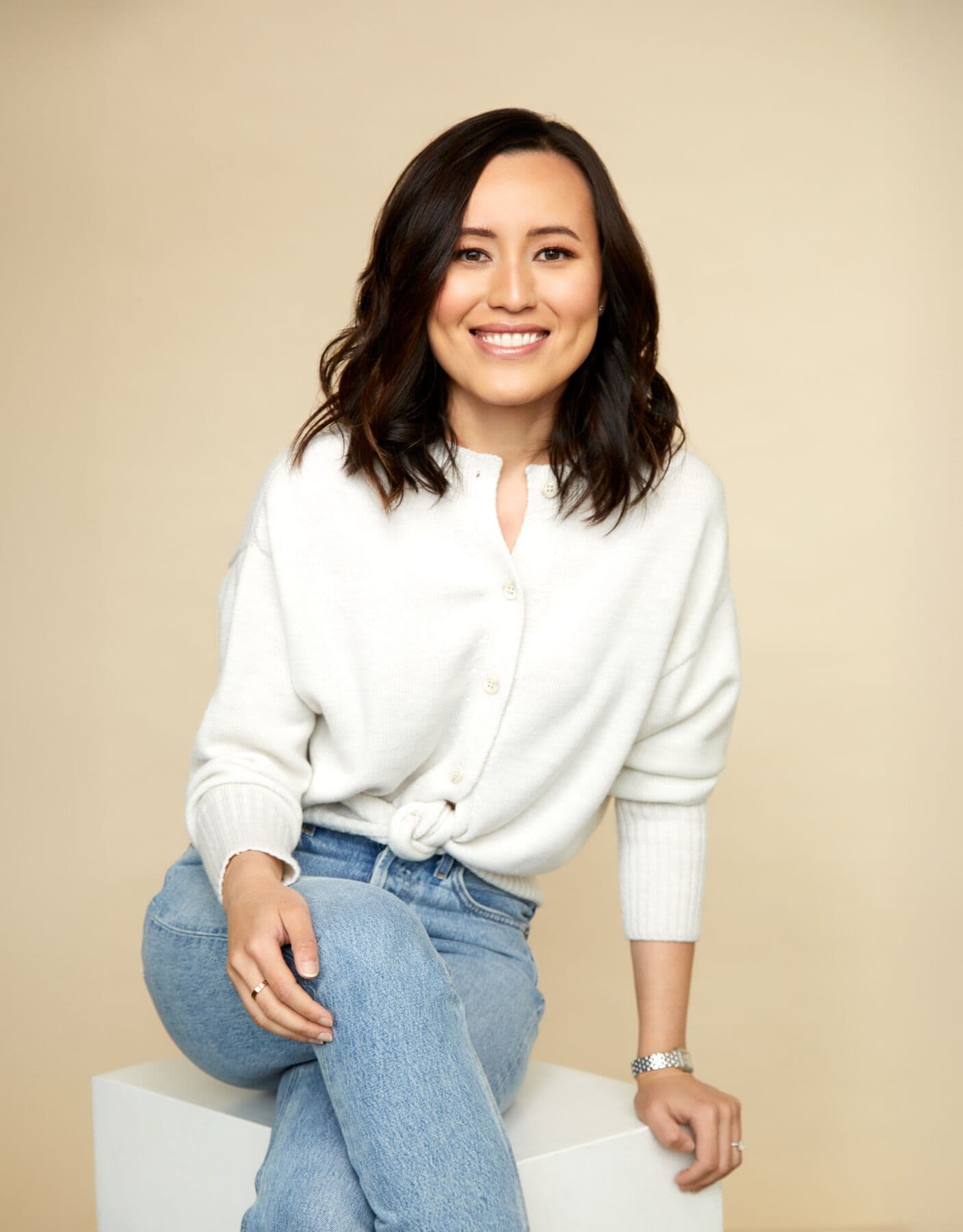 Gulinka, personal stylist, seated in a white cardigan and jeans